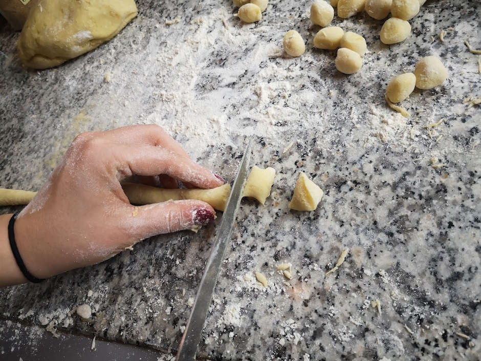 Gnocci schneiden, Hand mit roten Fingernägeln auf Steinplatte mit Mehl bestäubt.